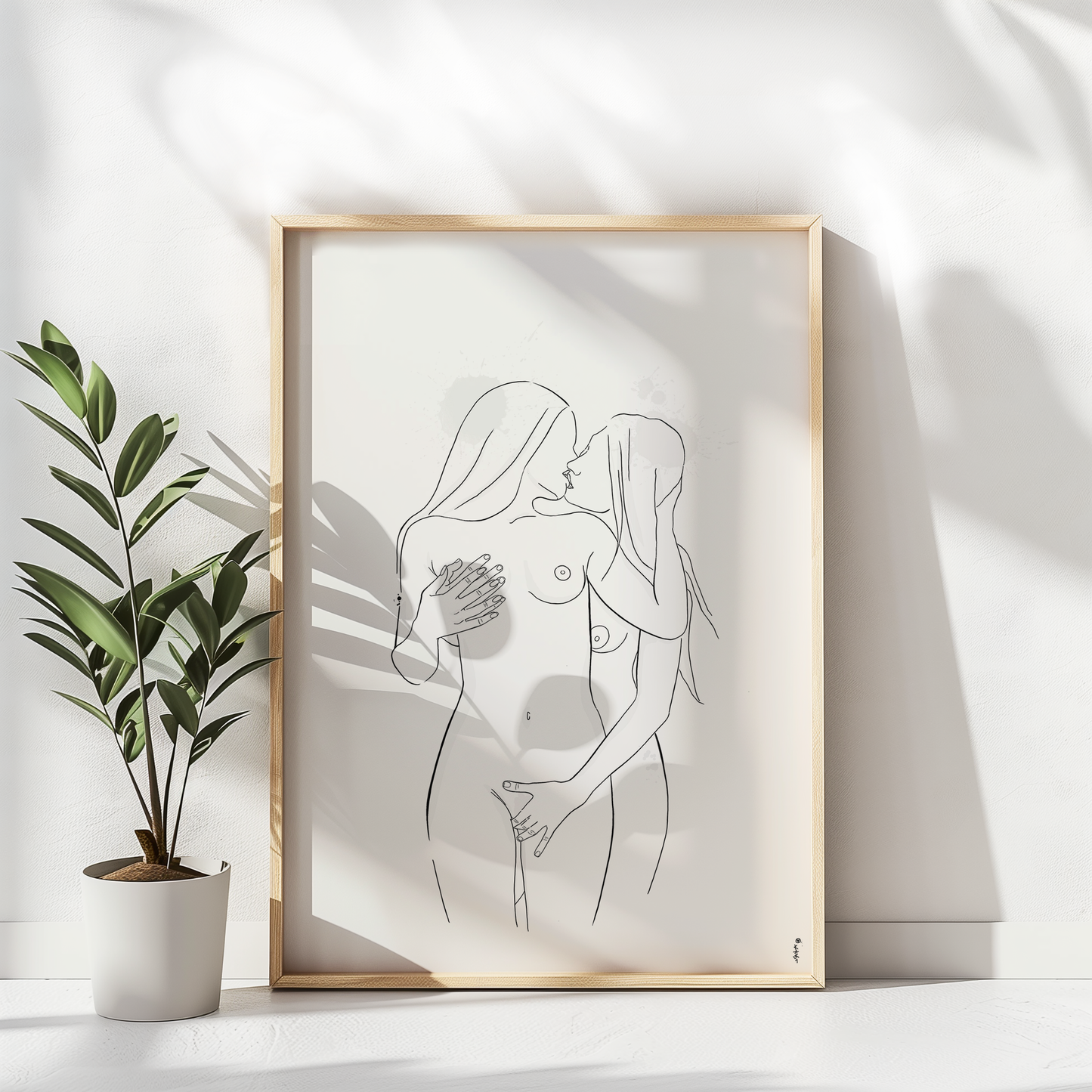 Mockup displaying erotic art of 2 nude women, in natural wooden frame on white floor with a plant on the right