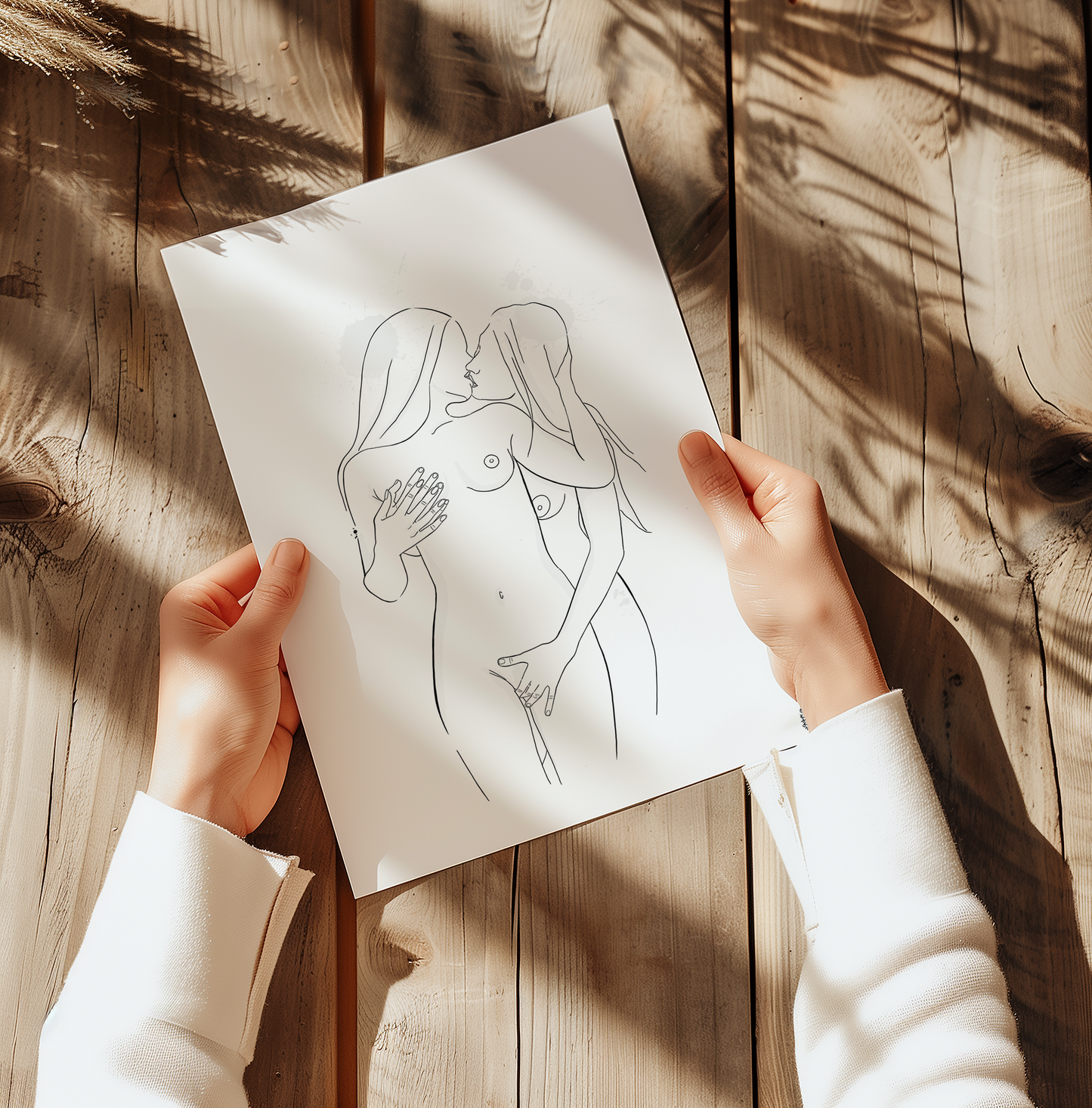 Mockup displaying erotic art of 2 nude women, placed on a wooden table with a woman holding the print